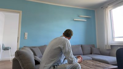 Mann sitzt auf Sofa. Er ist von hinten zu sehen